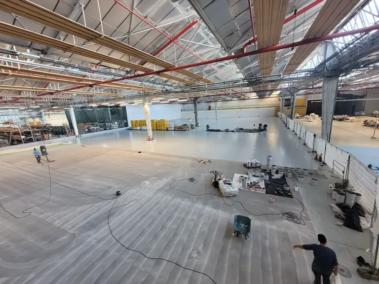 Chantier de revêtement de sol industriel en résine dans un vaste bâtiment, avec zone de travaux et opérateurs — CGS France.
