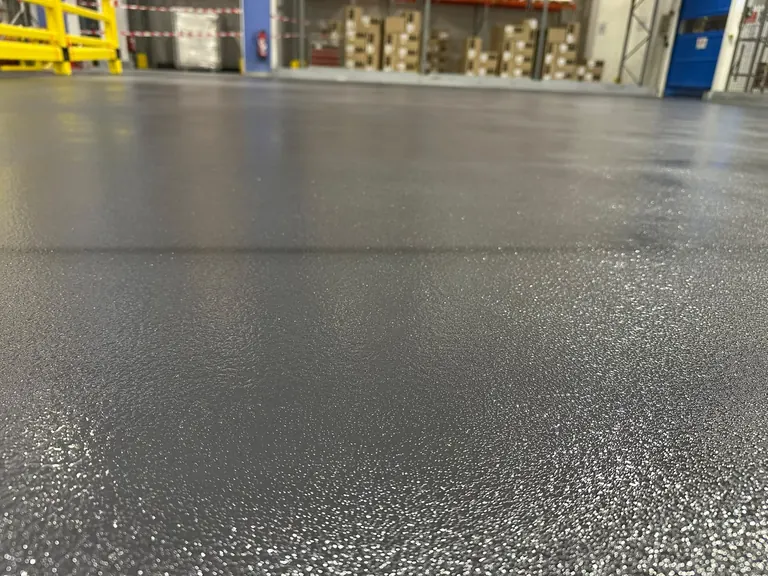 Vue rapprochée d’un revêtement de sol industriel en résine quartz color avec nuances de gris présentant une finition texturée — CGS France.