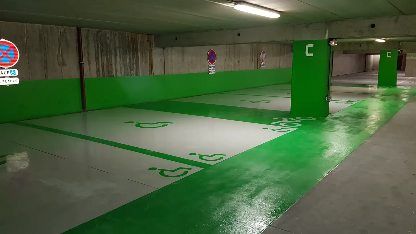 Parking souterrain avec revêtement de sol en résine, places PMR, pictogrammes handicap et marquage vert — CGS France.