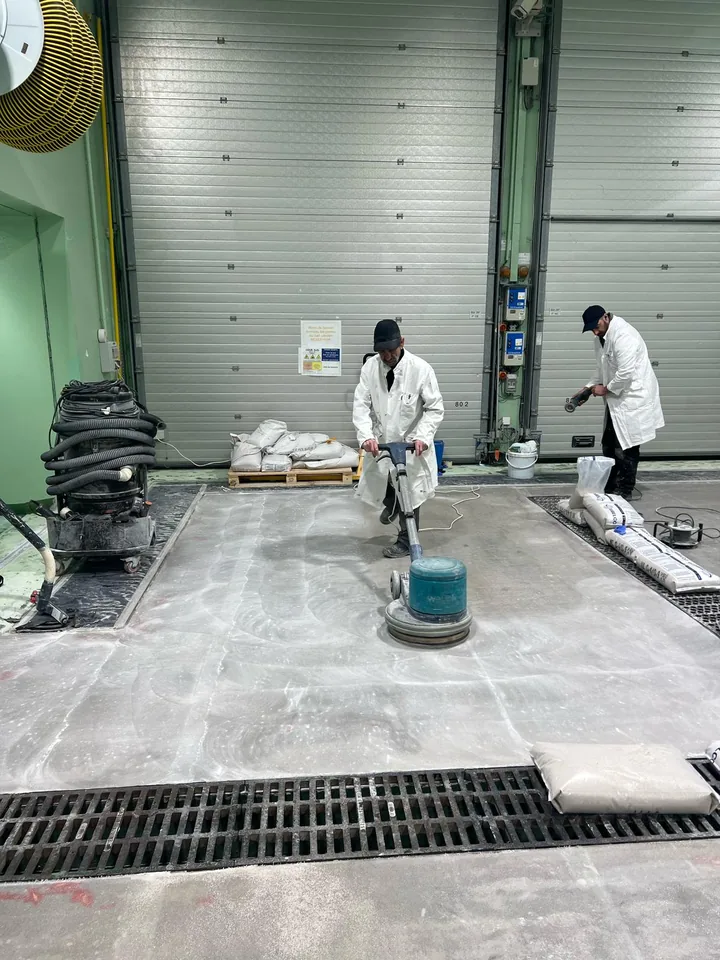 Opérateurs préparant le sol industriel avec une machine de ponçage.