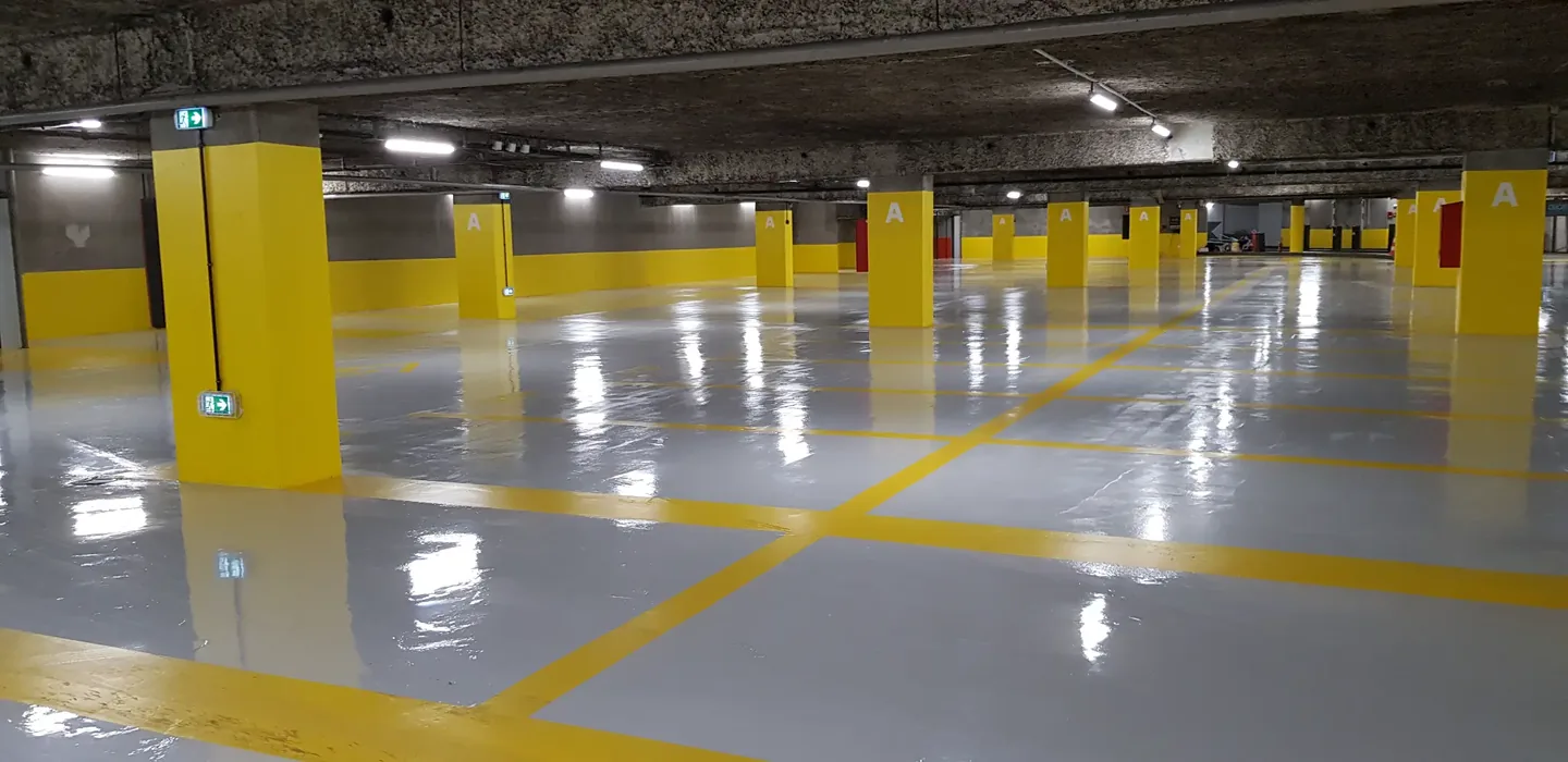 Parking couvert avec sol gris, marquages jaunes et poteaux assortis
