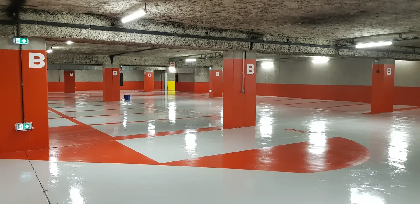 Parking souterrain rénové avec sol en résine gris et orange, marquage des voies de circulation et poteaux de signalisation — CGS France.