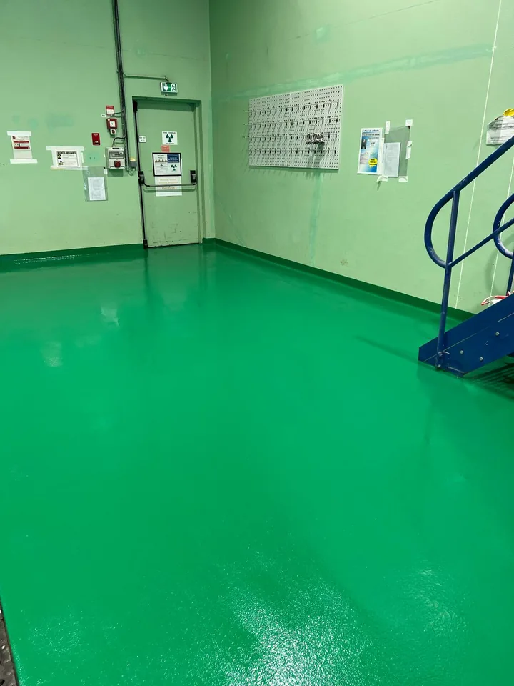Détail de la finition du sol vert en résine près du mur et de l’escalier.